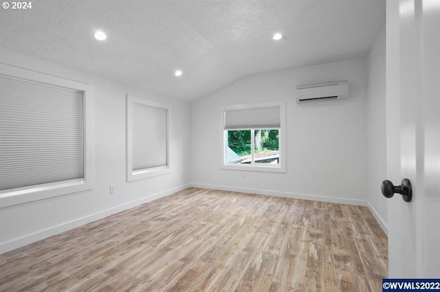 spare room with an AC wall unit, vaulted ceiling, light hardwood / wood-style floors, and a textured ceiling