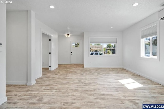 entryway with an AC wall unit, light hardwood / wood-style flooring, and a textured ceiling