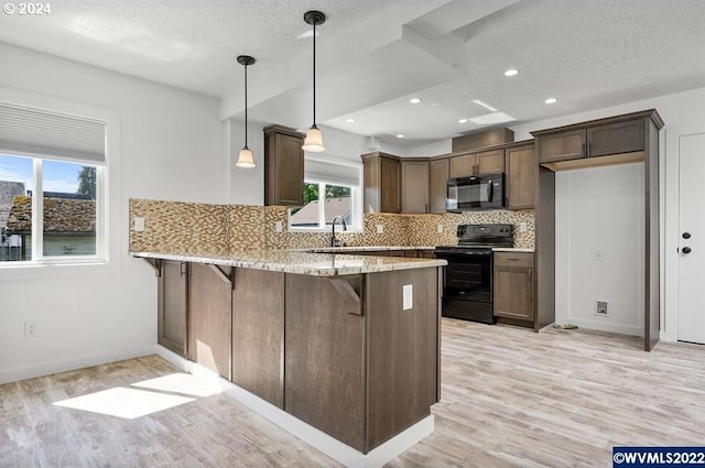 kitchen with black appliances, light wood-type flooring, hanging light fixtures, a breakfast bar area, and kitchen peninsula