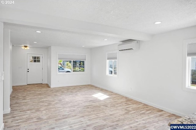 spare room with beam ceiling, a textured ceiling, a wall mounted air conditioner, and light hardwood / wood-style flooring