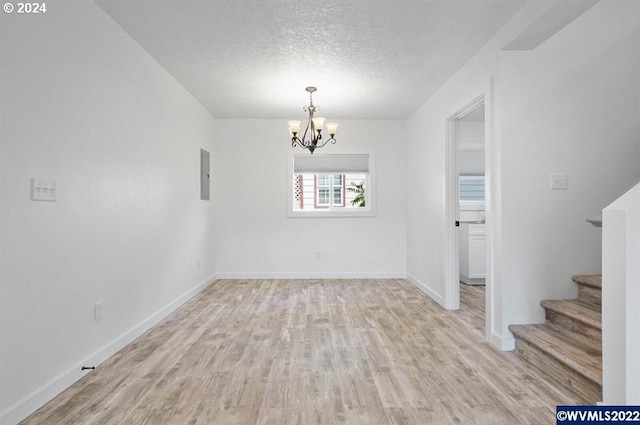 empty room with electric panel, a chandelier, a textured ceiling, and light hardwood / wood-style floors