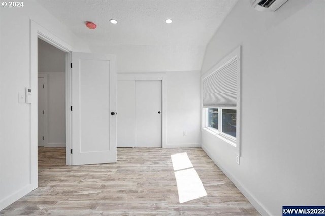 spare room featuring a wall unit AC, a textured ceiling, and light wood-type flooring