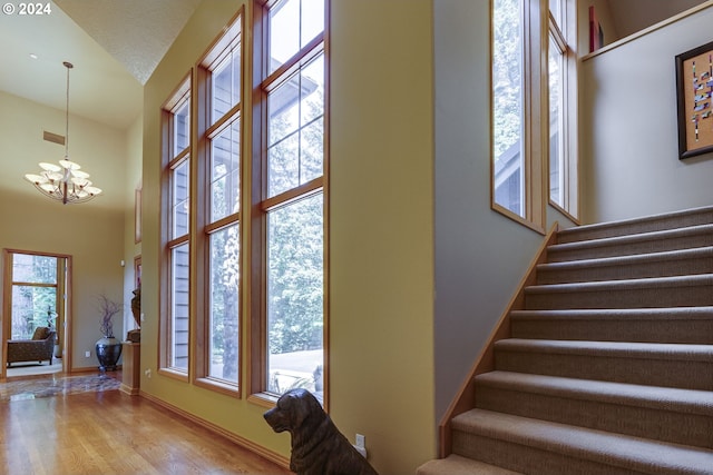 stairway featuring a notable chandelier, a high ceiling, a wealth of natural light, and wood finished floors