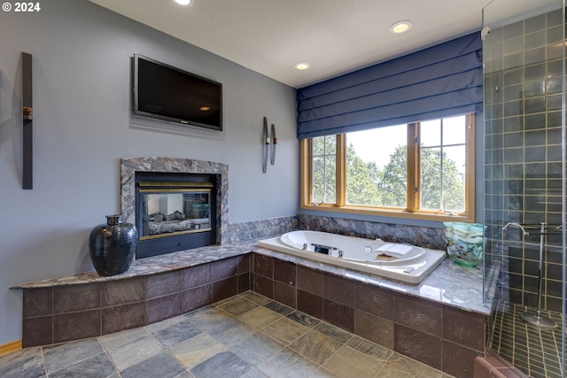 bathroom with recessed lighting, stone finish flooring, a garden tub, and a premium fireplace