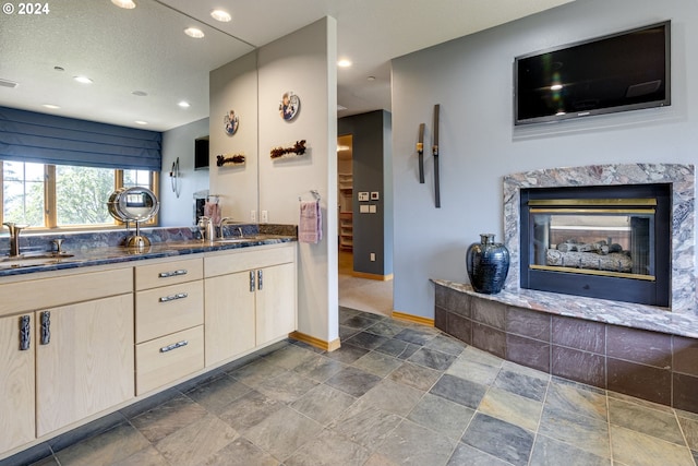 kitchen featuring baseboards, a premium fireplace, dark stone countertops, a sink, and recessed lighting