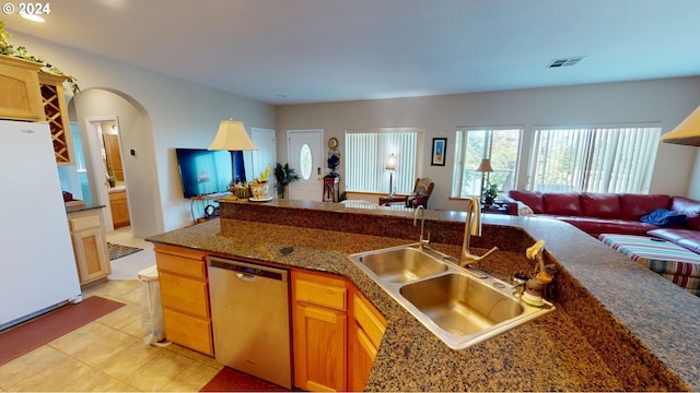 kitchen with open floor plan, dishwasher, freestanding refrigerator, arched walkways, and a sink