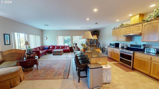 kitchen with under cabinet range hood, open floor plan, a breakfast bar area, appliances with stainless steel finishes, and a sink