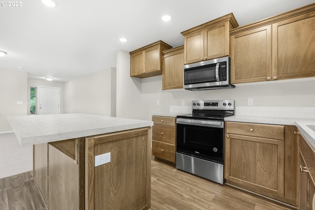 kitchen featuring recessed lighting, stainless steel appliances, light countertops, light wood-type flooring, and brown cabinets