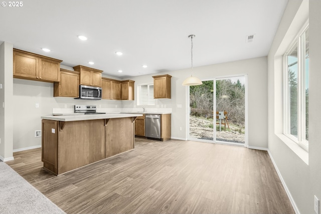 kitchen with stainless steel appliances, brown cabinetry, light countertops, and pendant lighting