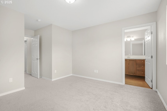 unfurnished bedroom with baseboards, ensuite bathroom, a sink, and light colored carpet