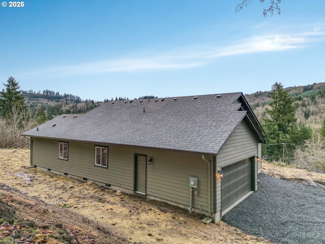 rear view of property with crawl space, a shingled roof, and a garage