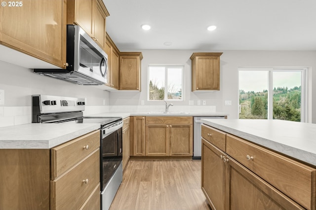 kitchen with stainless steel appliances, light countertops, light wood-style floors, brown cabinetry, and a sink