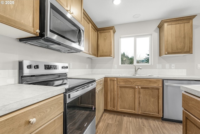 kitchen with brown cabinets, light countertops, light wood-style flooring, appliances with stainless steel finishes, and a sink