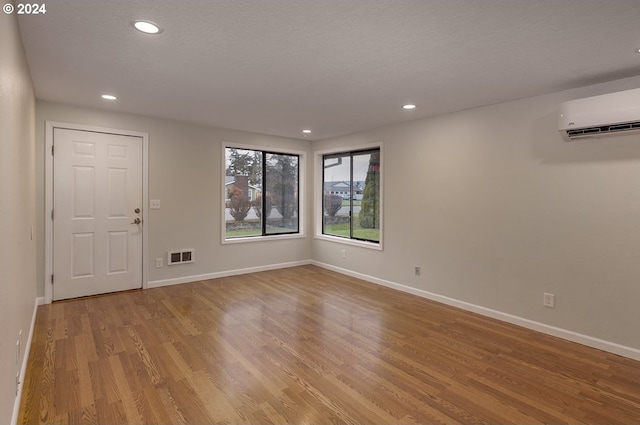 empty room featuring a textured ceiling, light wood-type flooring, and an AC wall unit