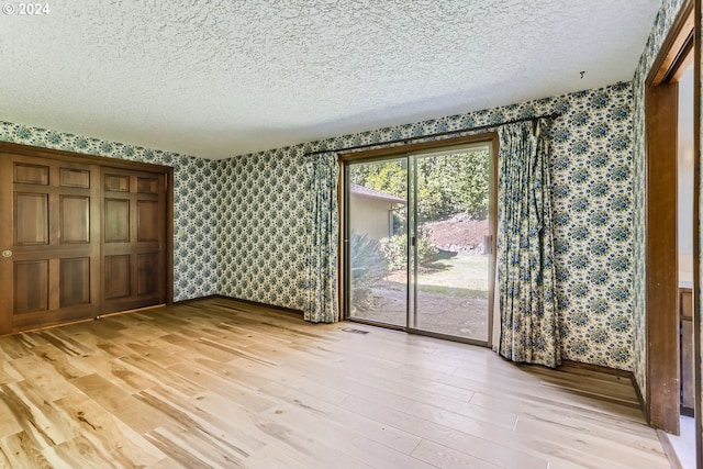 unfurnished bedroom featuring access to exterior, light hardwood / wood-style floors, and a textured ceiling