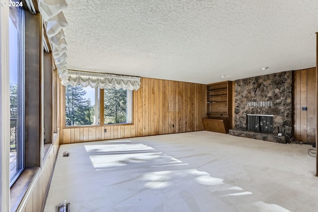 unfurnished living room with a textured ceiling, a fireplace, wood walls, and carpet flooring