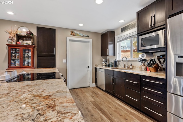 kitchen with sink, dark brown cabinetry, appliances with stainless steel finishes, light stone counters, and light hardwood / wood-style floors