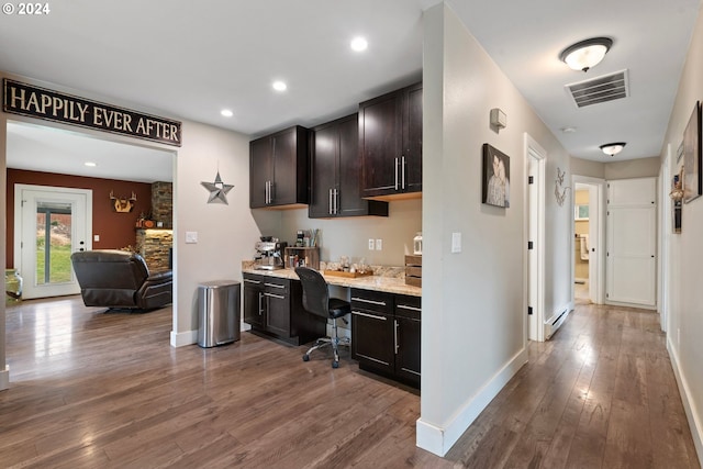 kitchen featuring built in desk, dark brown cabinets, a baseboard radiator, light stone countertops, and hardwood / wood-style flooring