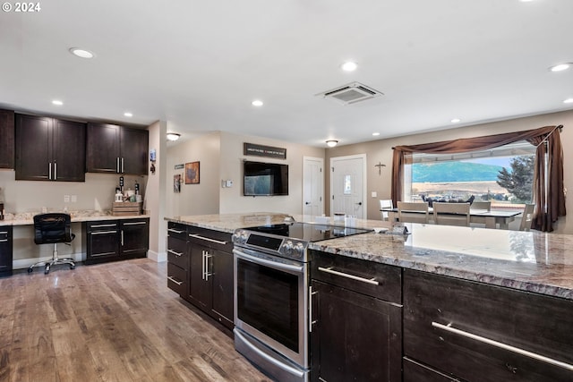 kitchen featuring built in desk, electric range, light wood-type flooring, dark brown cabinetry, and light stone counters