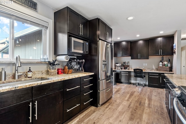 kitchen featuring built in desk, sink, dark brown cabinetry, light wood-type flooring, and appliances with stainless steel finishes