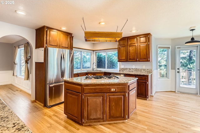 kitchen featuring pendant lighting, a center island, stainless steel appliances, light stone countertops, and light wood-type flooring