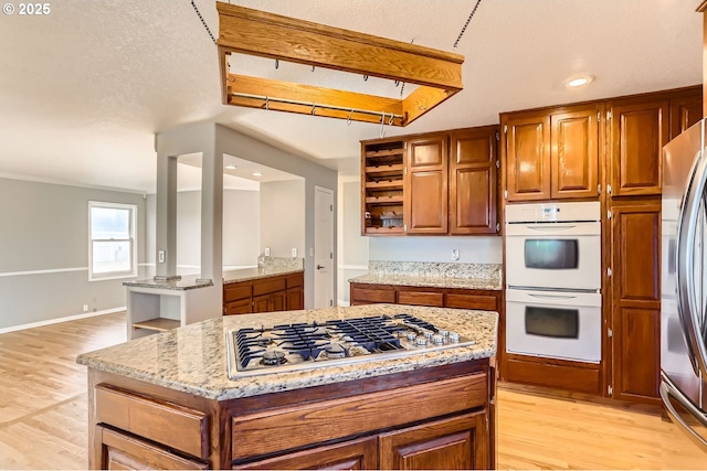 kitchen with a center island, light hardwood / wood-style floors, stainless steel appliances, light stone countertops, and a textured ceiling