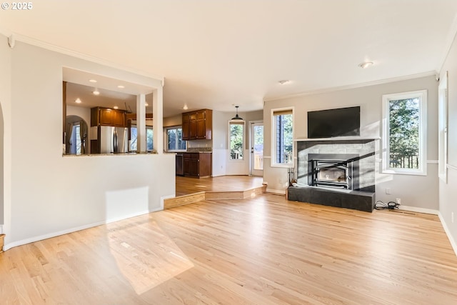 unfurnished living room with ornamental molding, a tiled fireplace, and light hardwood / wood-style floors