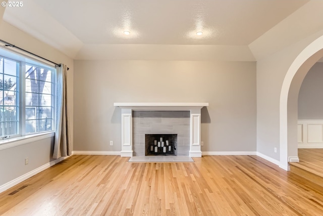 unfurnished living room with a tiled fireplace, light hardwood / wood-style flooring, and lofted ceiling