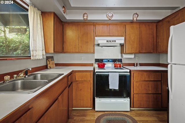 kitchen with a sink, brown cabinetry, white appliances, light countertops, and under cabinet range hood