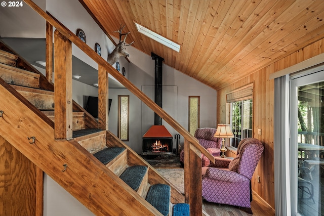 living area featuring vaulted ceiling with skylight, wood finished floors, wood ceiling, wooden walls, and a wood stove