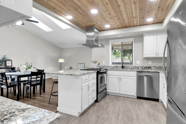 kitchen with a peninsula, island range hood, white cabinets, appliances with stainless steel finishes, and a skylight