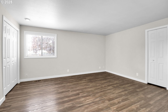 unfurnished bedroom featuring baseboards, dark wood-style flooring, and visible vents