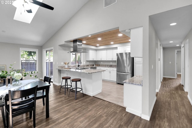 kitchen with freestanding refrigerator, a peninsula, island exhaust hood, wood finished floors, and visible vents