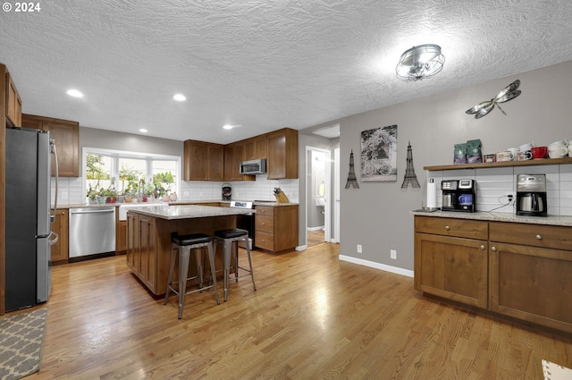 kitchen featuring light wood-type flooring, a textured ceiling, stainless steel appliances, a kitchen island, and a breakfast bar area