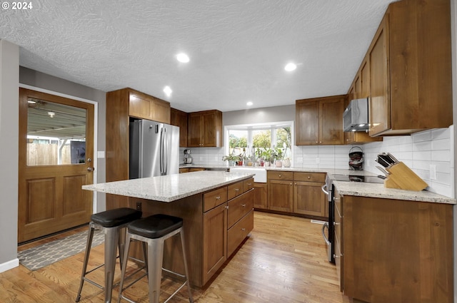 kitchen featuring backsplash, stainless steel appliances, light hardwood / wood-style flooring, a kitchen island, and a breakfast bar area