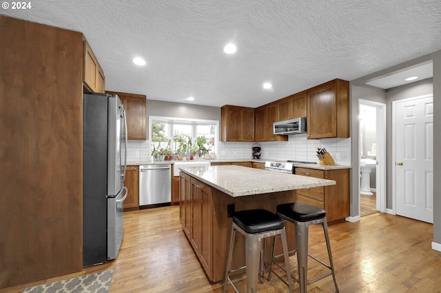 kitchen with light stone counters, a breakfast bar, stainless steel appliances, light hardwood / wood-style flooring, and a kitchen island