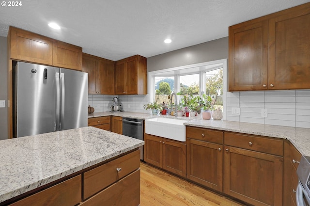 kitchen with sink, light stone countertops, light wood-type flooring, tasteful backsplash, and stainless steel appliances