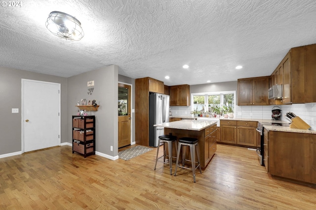 kitchen featuring a center island, backsplash, a kitchen bar, appliances with stainless steel finishes, and light wood-type flooring