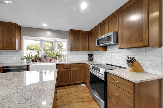 kitchen with decorative backsplash, light hardwood / wood-style flooring, stainless steel appliances, and a textured ceiling