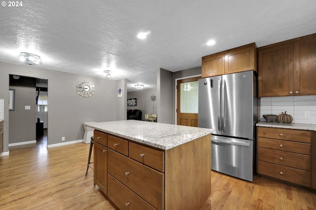 kitchen featuring stainless steel fridge, light hardwood / wood-style floors, a textured ceiling, a kitchen island, and a kitchen bar