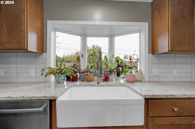 kitchen with backsplash, light stone counters, dishwasher, and sink