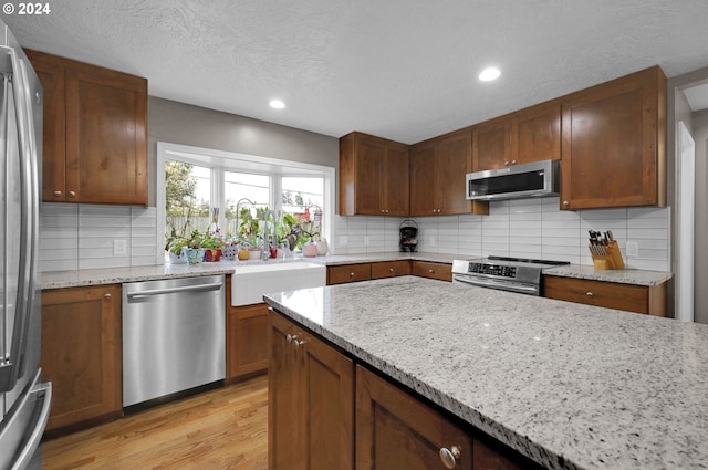 kitchen with backsplash, light wood-type flooring, a textured ceiling, appliances with stainless steel finishes, and light stone counters