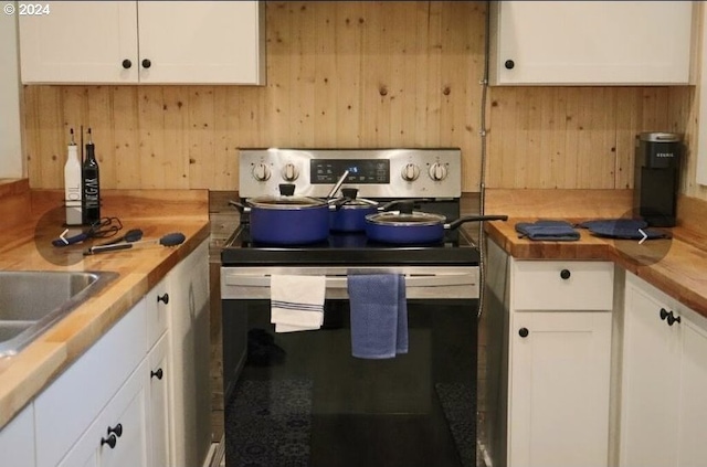 kitchen featuring white cabinetry, electric range, wooden walls, and butcher block countertops