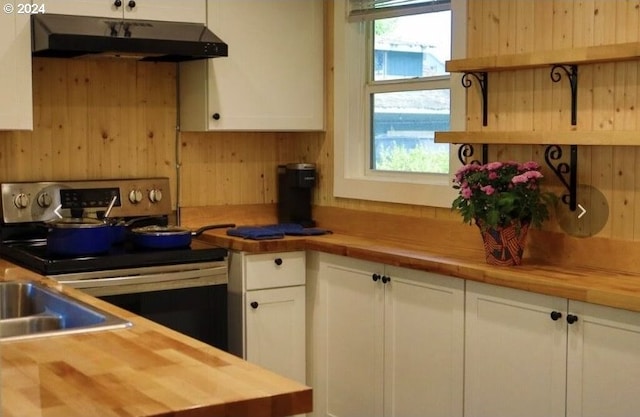 kitchen featuring wooden walls, electric range, under cabinet range hood, white cabinetry, and butcher block counters