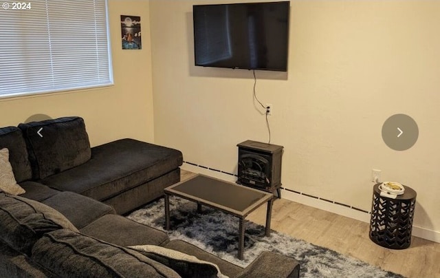 living room with a baseboard heating unit, wood finished floors, and a wood stove