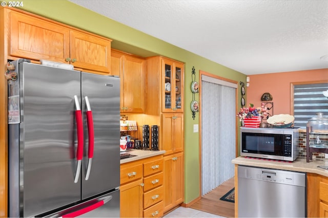 3824 Brighton Ave, Eugene, OR 97405 - kitchen featuring appliances with stainless steel finishes, light countertops, light tile patterned flooring, glass insert cabinets, and a textured ceiling