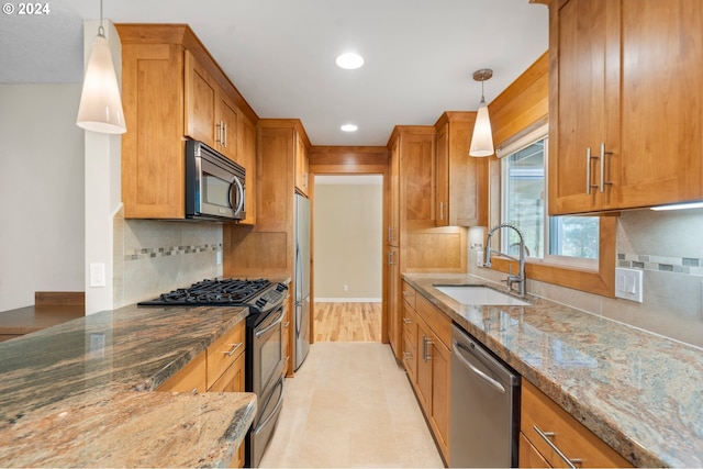 kitchen with appliances with stainless steel finishes, decorative light fixtures, dark stone counters, and sink