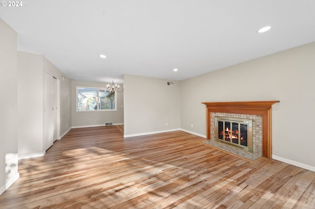 unfurnished living room featuring a tiled fireplace, light hardwood / wood-style flooring, and a chandelier