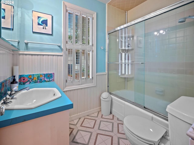 full bathroom featuring tile patterned floors, a wainscoted wall, toilet, combined bath / shower with glass door, and vanity