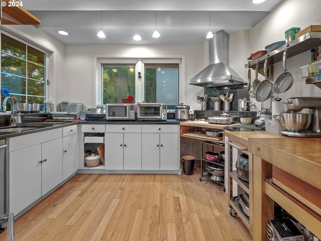 kitchen with range hood, backsplash, white cabinetry, light hardwood / wood-style flooring, and pendant lighting